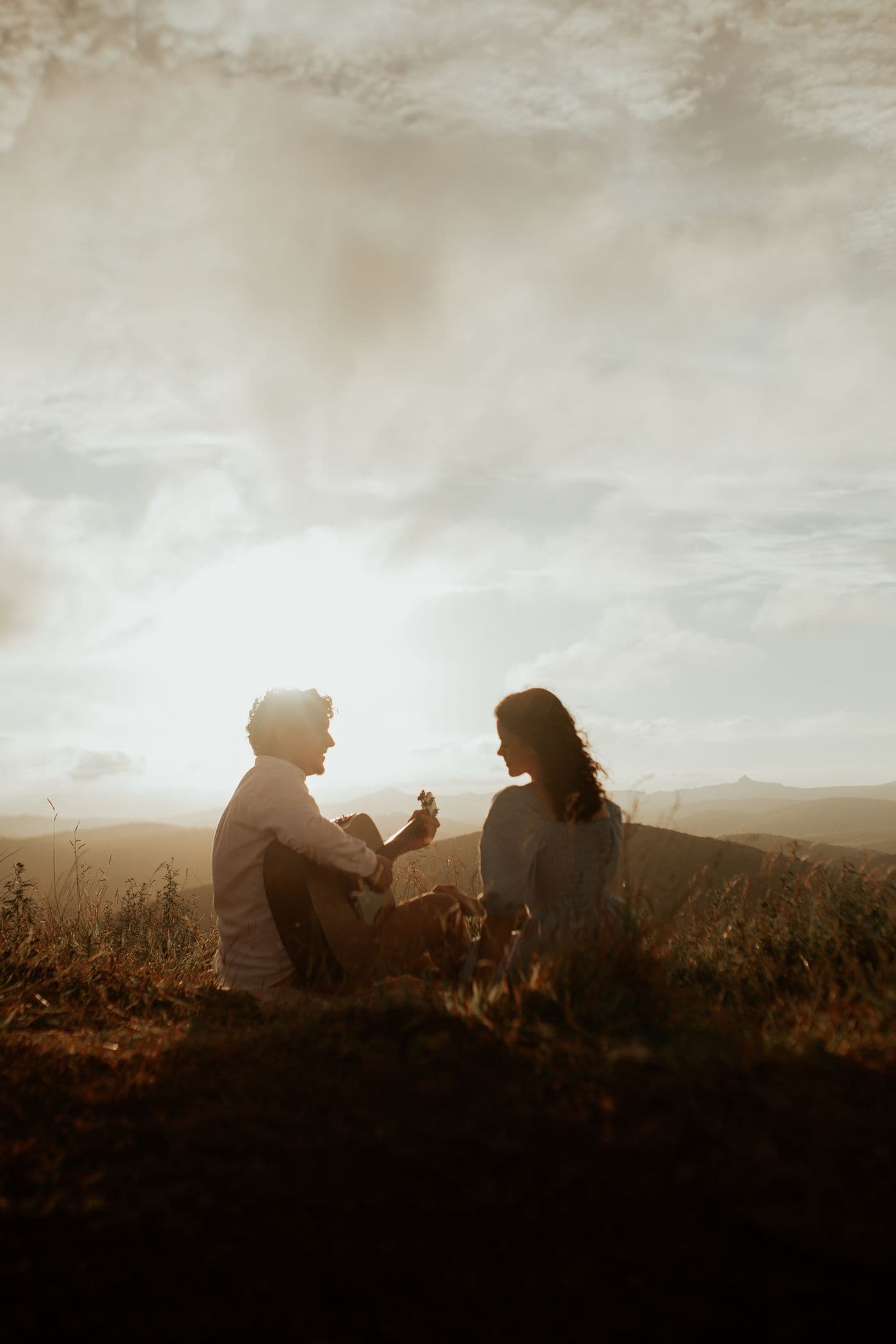Casal sentado tocando violão ao pôr do sol